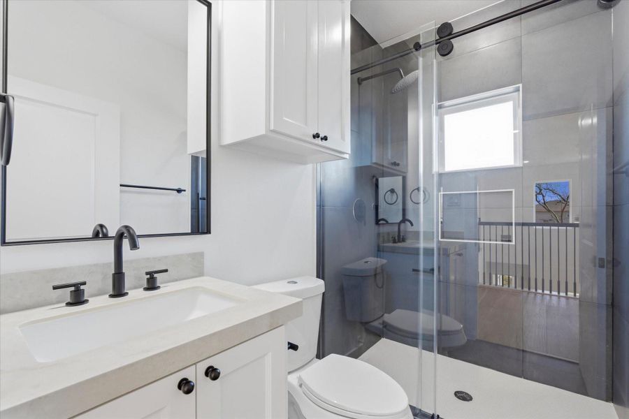 The second bath upstairs is thoughtfully designed with a glass-enclosed walk-in shower featuring sliding doors, complemented by additional built-in cabinet storage.