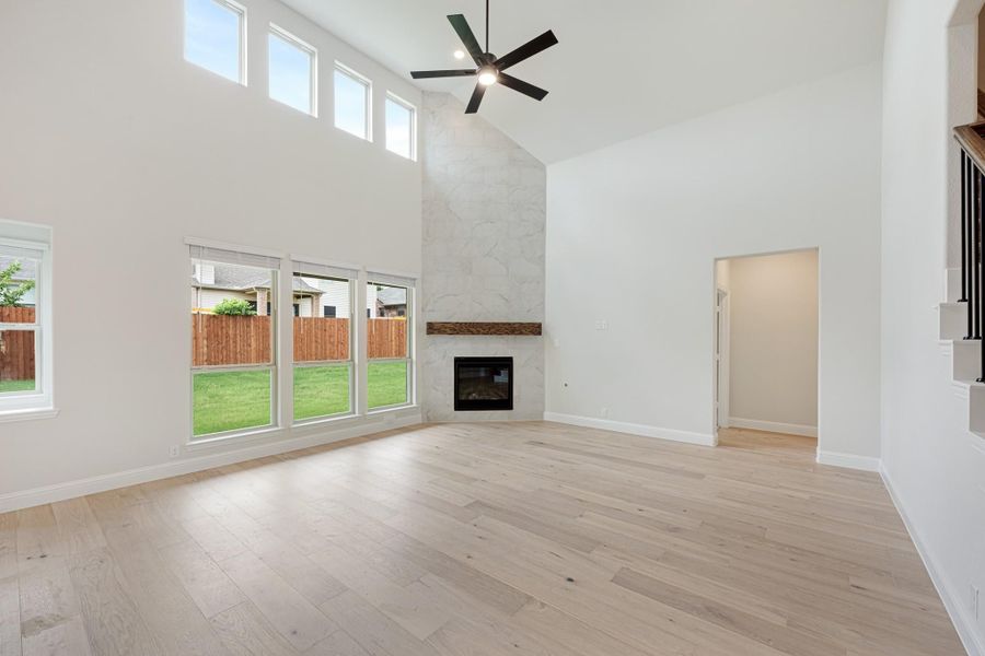 Open living room with vaulted ceiling, marble fireplace, ceiling fan, and light hardwood floors Open living room with vaulted ceiling, marble fireplace, ceiling fan, and light hardwood floors