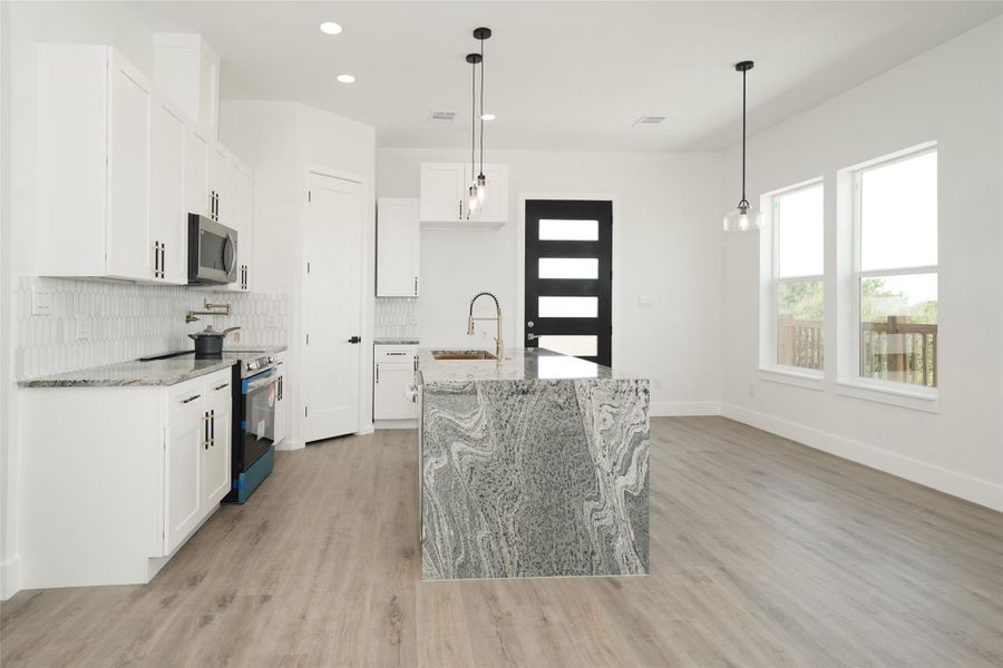 This kitchen features sleek white cabinetry with modern black handles, a stainless steel microwave, and a stove. The countertops have a stylish granite finish, complemented by a geometric tile backsplash. The room has a clean and contemporary feel, ideal for any home buyer.