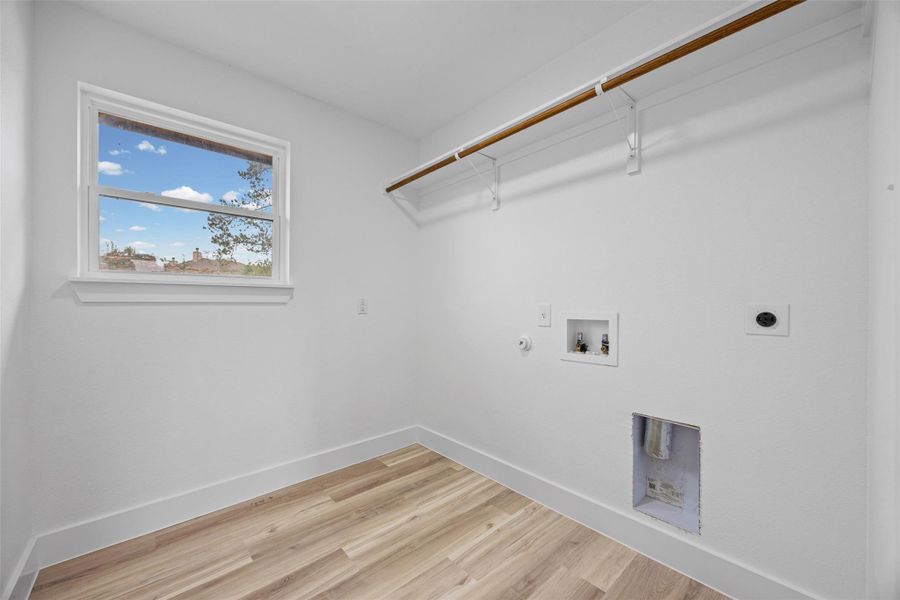 Dedicated utility room located upstairs featuring wood-finish flooring, a single window, white walls, and a built-in hanging rod with shelving brackets Dedicated utility room located upstairs featuring wood-finish flooring, a single window, white walls, and a built-in hanging rod with shelving brackets