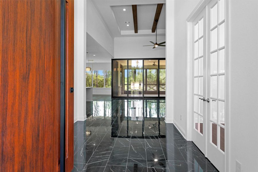 A dramatic entryway sets the tone with sleek black marble tile, soaring ceilings with wood beams, and a wall of glass showcasing serene wooded views beyond the screened patio. A dramatic entryway sets the tone with sleek black marble tile, soaring ceilings with wood beams, and a wall of glass showcasing serene wooded views beyond the screened patio.