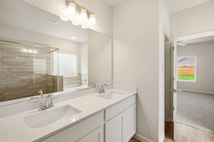 The elegant double vanity in the primary bathroom boasts quartz countertops, chrome fixtures, and sleek cabinetry, providing functionality with a luxurious feel. A large mirror and bright lighting complete this modern design.