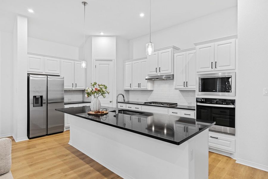 Kitchen with stainless steel appliances, a center island with sink, backsplash, light wood-type flooring, and white cabinets