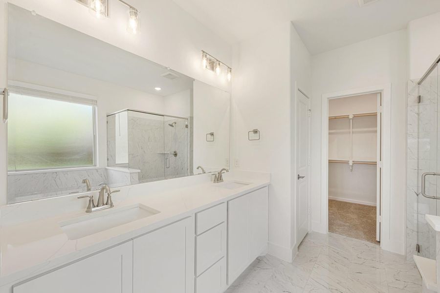 Master bathroom with double vanity, white cabinets, glass shower, and walk-in closet entrance