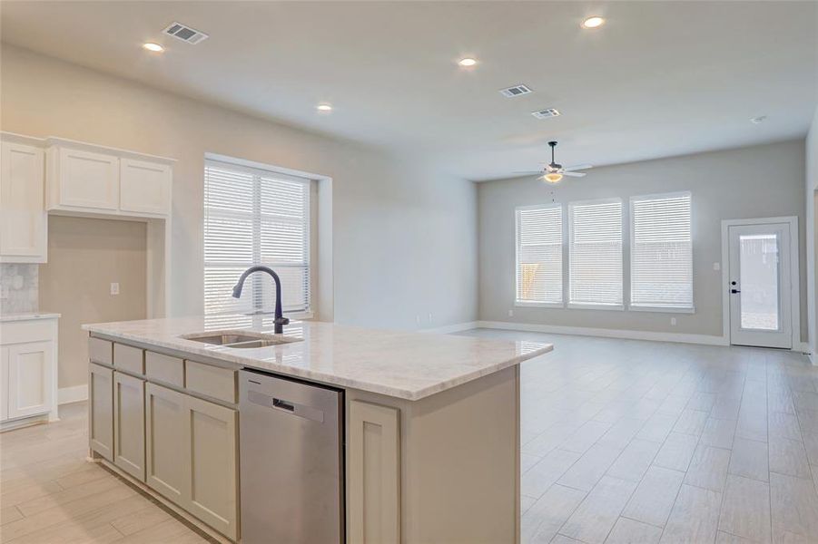 Kitchen with sink, stainless steel dishwasher, light stone countertops, a center island with sink, and light wood-type flooring