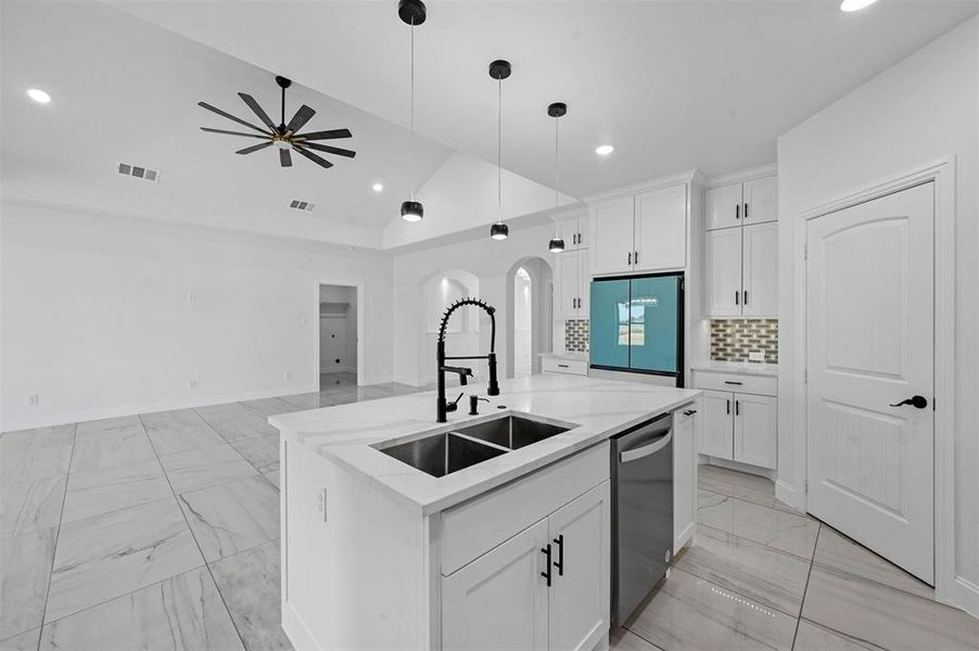 Kitchen with vaulted ceiling, appliances with stainless steel finishes, white cabinetry, sink, and a center island with sink