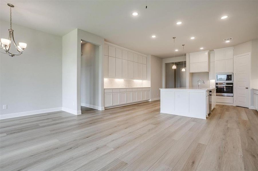 Kitchen with light hardwood / wood-style floors, appliances with stainless steel finishes, white cabinets, and a center island with sink