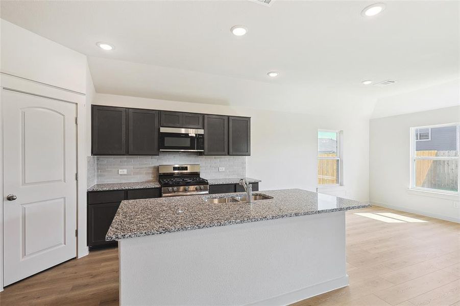 Kitchen featuring light hardwood / wood-style floors, a center island with sink, sink, backsplash, and appliances with stainless steel finishes