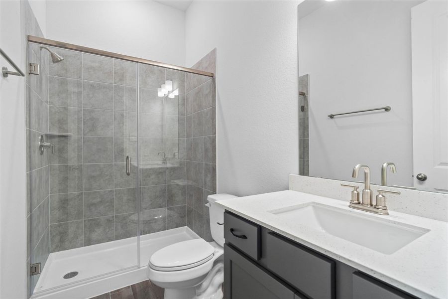 This secondary bathroom features a framed and spacious walk-in shower with tile surround, wood-look tile flooring, vanity with a stunning light countertop, mirror, sleek brushed nickel fixtures, and contemporary finishes throughout. This secondary bathroom features a framed and spacious walk-in shower with tile surround, wood-look tile flooring, vanity with a stunning light countertop, mirror, sleek brushed nickel fixtures, and contemporary finishes throughout.