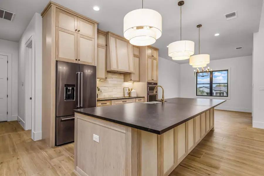 Kitchen with visible vents, dark countertops, high quality fridge, decorative light fixtures, and light brown cabinetry