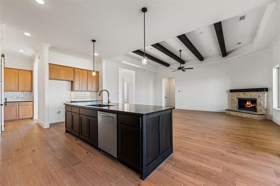 Kitchen featuring open floor plan, an island with sink, hanging light fixtures, crown molding, and dishwasher