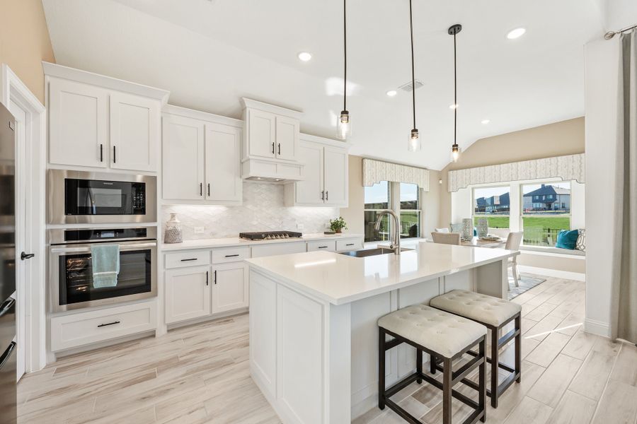 Kitchen with white cabinets, large island with seating, stainless steel appliances, and pendant lights