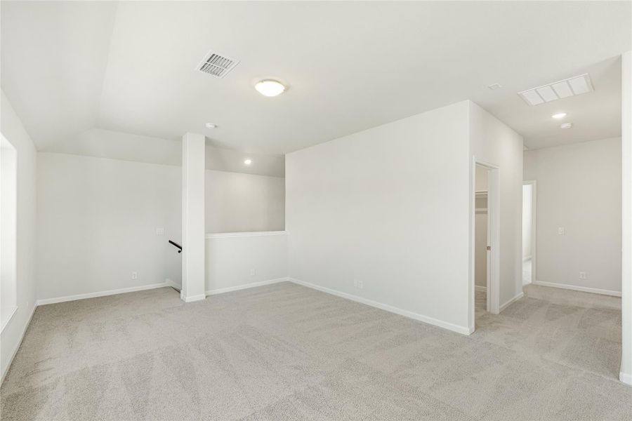 Empty upstairs loft or bonus room with gray carpet, white walls, and staircase railing visible in background