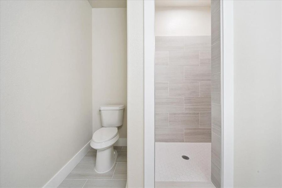 Bathroom with a tile shower, tile patterned floors, and toilet