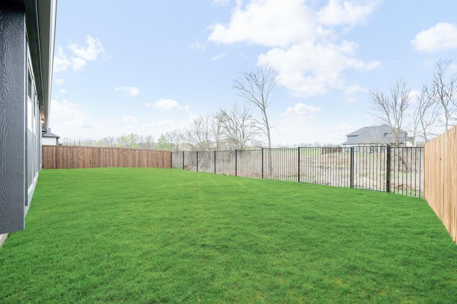 Spacious backyard with green lawn, wood privacy fence, and black metal fence along the side