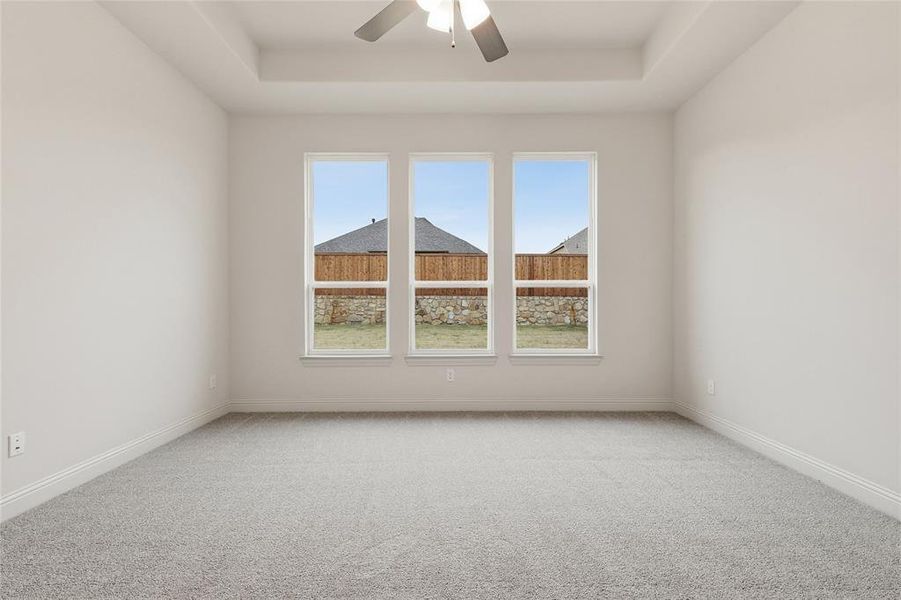 Unfurnished room featuring a tray ceiling, light carpet, and ceiling fan
