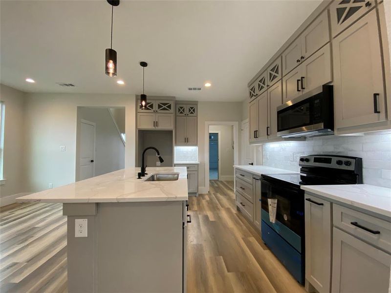 Kitchen with light wood-type flooring, black electric range oven, sink, an island with sink, and decorative backsplash