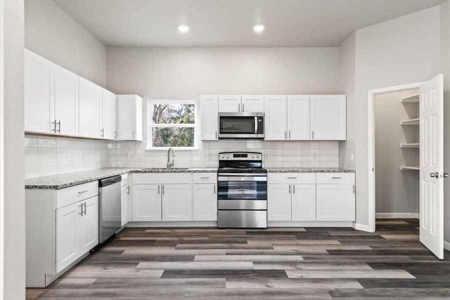 Gourmet kitchen with light stone countertops, white cabinetry, stainless steel appliances, and dark wood-type flooring