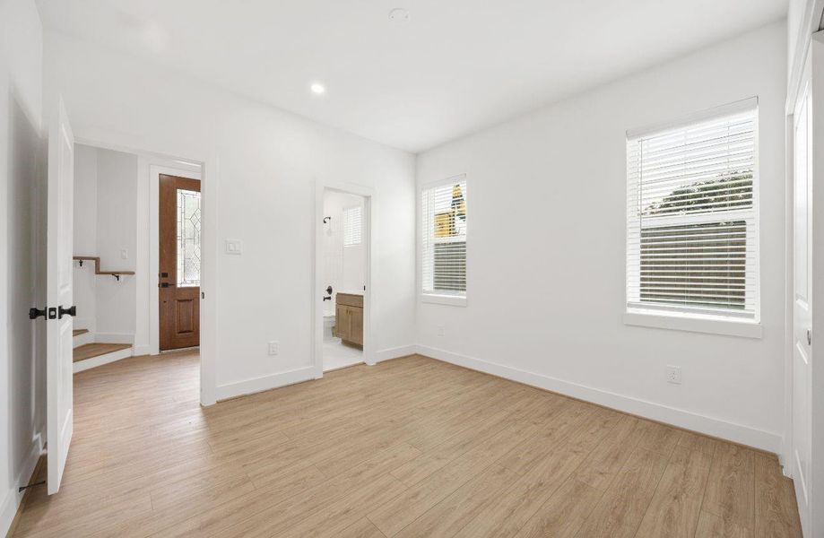 A spacious first-floor bedroom features natural light, neutral finishes, light wood-look flooring, and convenient access to a nearby full bath. With its clean design and flexible layout, this room is perfect for guests, work-from-home use, or a private retreat separate from the main living areas.