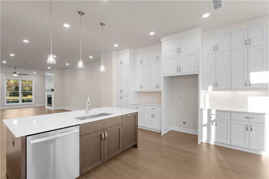 Kitchen with open floor plan, white cabinets, stainless steel dishwasher, a ceiling fan, and hanging light fixtures