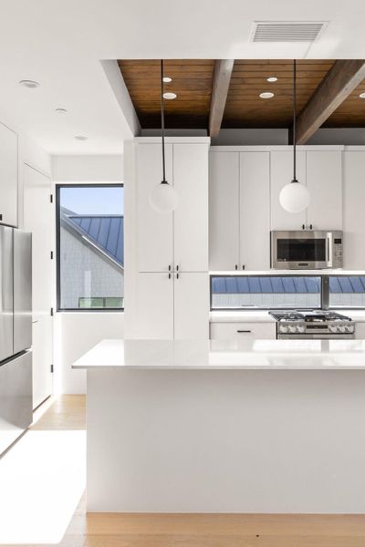 Kitchen featuring light wood-style flooring, a wood ceiling with exposed beams, decorative light fixtures, stainless steel appliances, and white cabinets