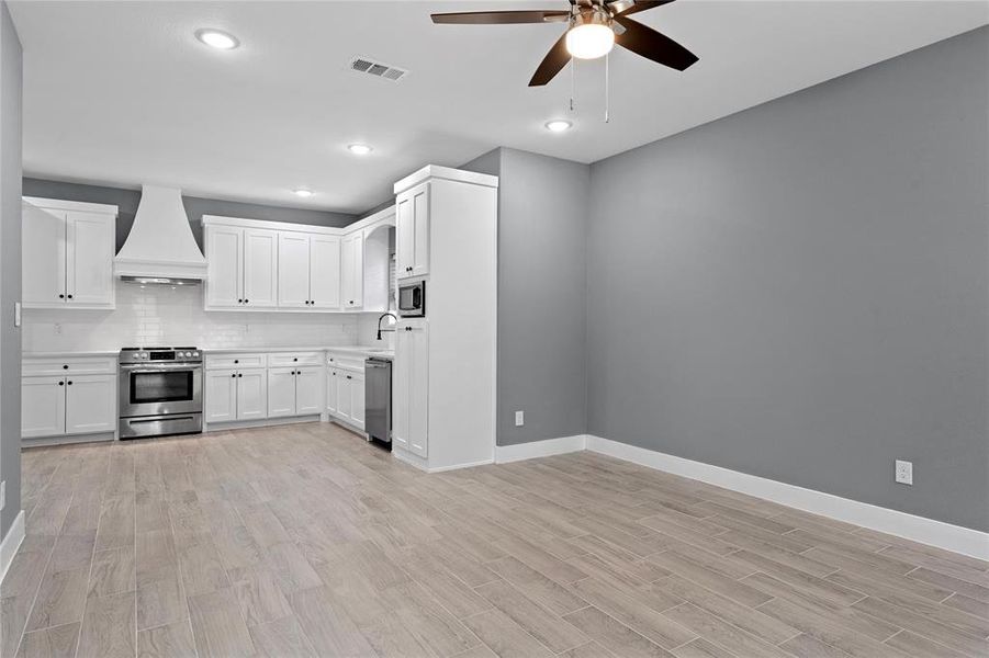 Kitchen featuring white cabinets, backsplash, light countertops, light wood-type flooring, and recessed lighting Kitchen featuring white cabinets, backsplash, light countertops, light wood-type flooring, and recessed lighting