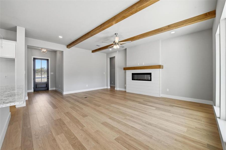 Unfurnished living room featuring beam ceiling, a glass covered fireplace, recessed lighting, light wood finished floors, and a ceiling fan Unfurnished living room featuring beam ceiling, a glass covered fireplace, recessed lighting, light wood finished floors, and a ceiling fan