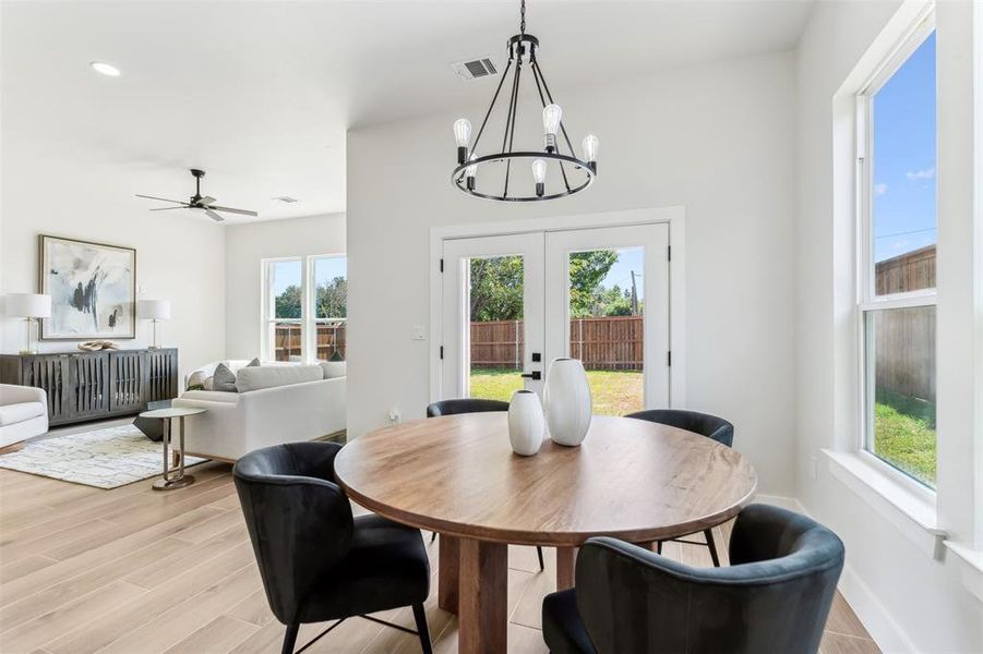 Dining room featuring light wood-type flooring, ceiling fan with notable chandelier, and french doors