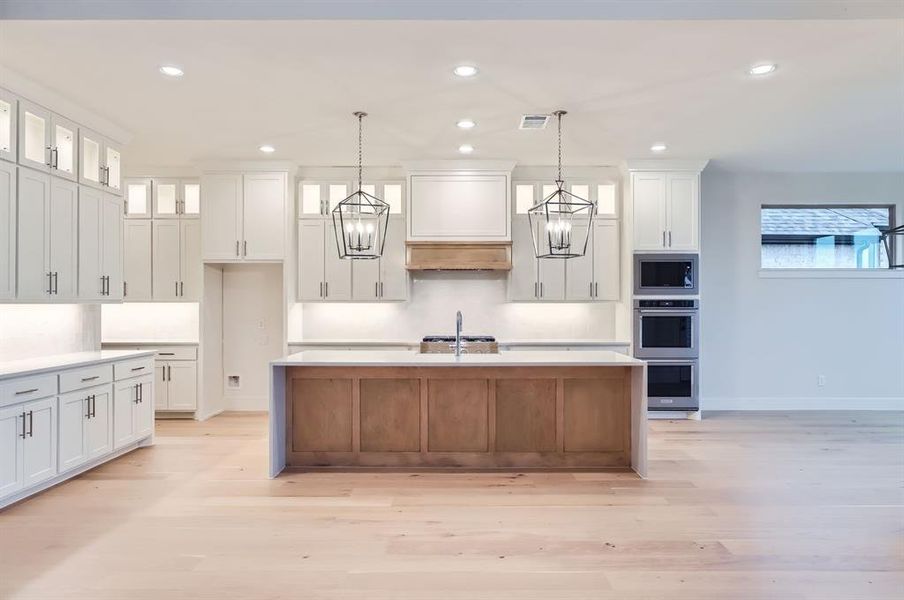 Kitchen with decorative light fixtures, white cabinetry, stainless steel appliances, and a center island with sink