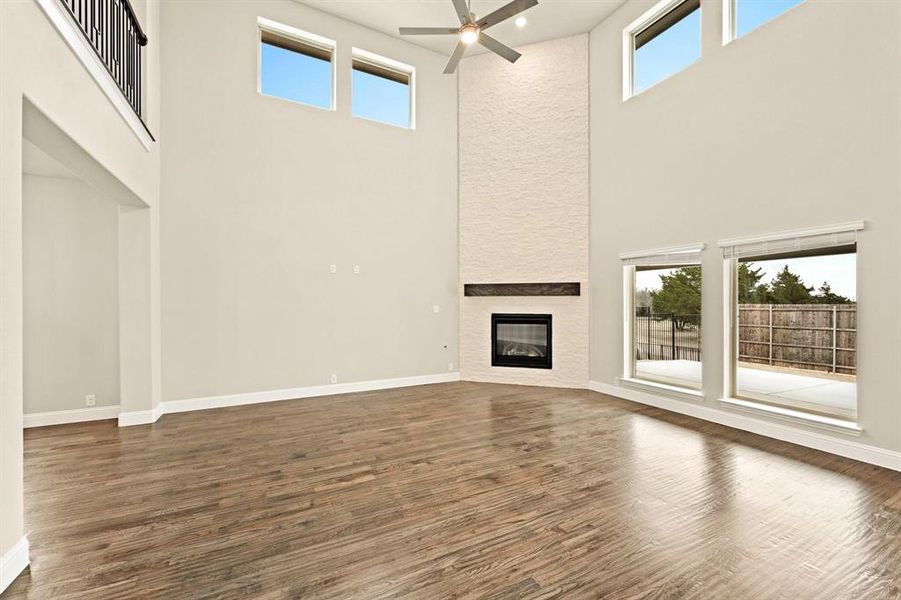 Unfurnished living room with a high ceiling, dark wood-type flooring, a large fireplace, and ceiling fan