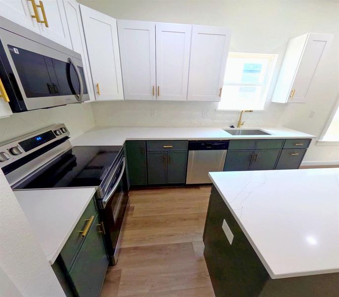 Kitchen featuring stainless steel appliances, white cabinetry, light wood finished floors, and green cabinets Kitchen featuring stainless steel appliances, white cabinetry, light wood finished floors, and green cabinets