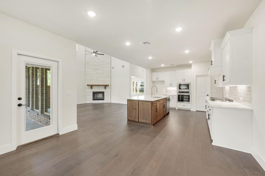 Open-concept kitchen and living area with white cabinets, wood island, stone fireplace, and dark hardwood floors