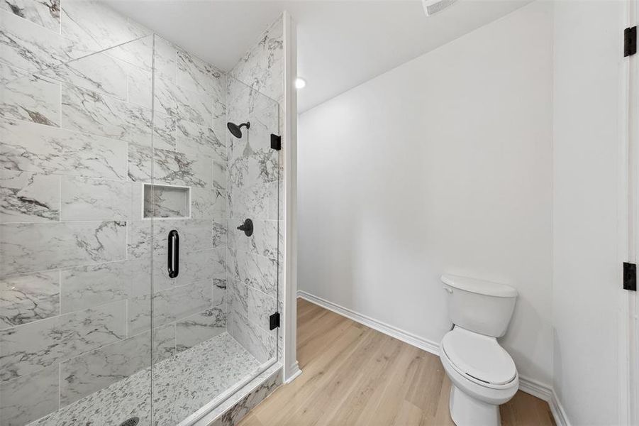 Bathroom with a marble finish shower, wood finished floors, and recessed lighting