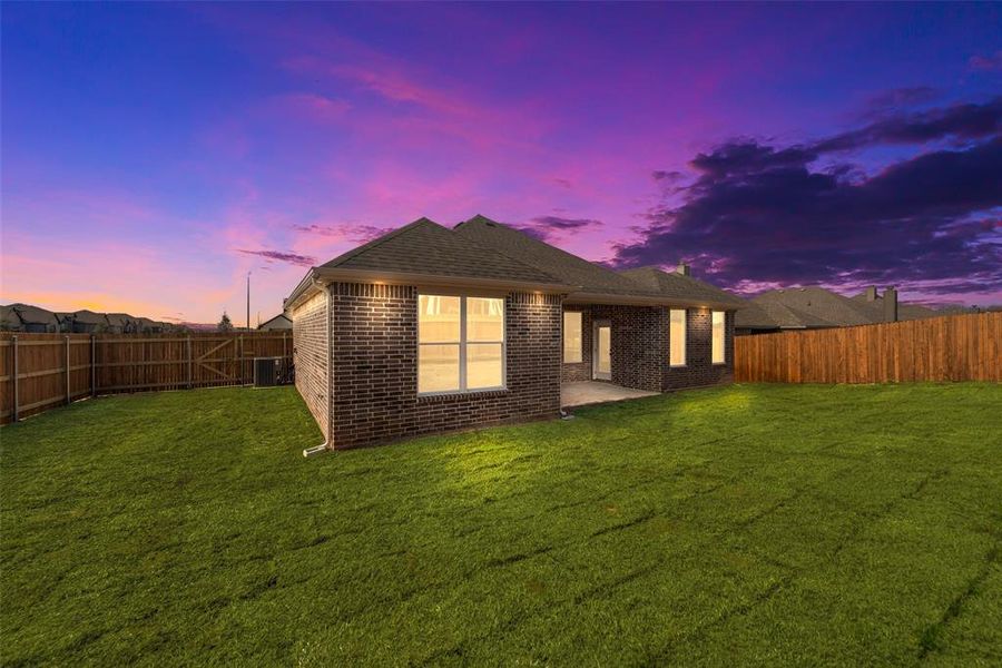 Back house at dusk featuring a yard and a patio area