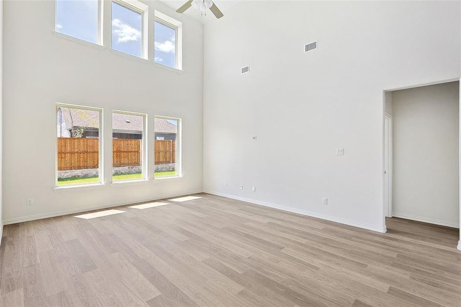 Empty room featuring light wood-type flooring, a towering ceiling, and ceiling fan