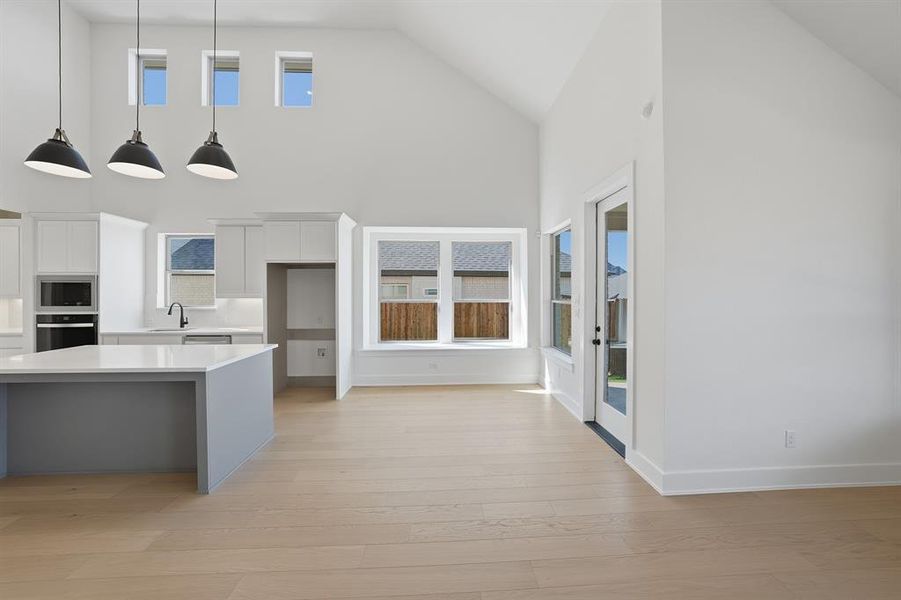 Kitchen with white cabinets, stainless steel appliances, decorative light fixtures, high vaulted ceiling, and light wood finished floors Kitchen with white cabinets, stainless steel appliances, decorative light fixtures, high vaulted ceiling, and light wood finished floors