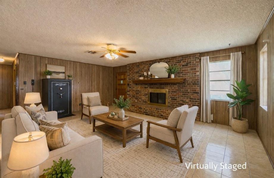 Living room featuring wooden walls, ceiling fan, a brick fireplace, a textured ceiling, and light tile patterned floors