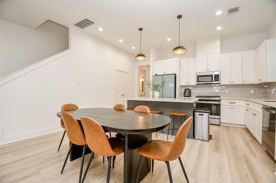 Modern kitchen and dining area with sleek white cabinetry, stainless steel appliances and center island makes a warm and inviting space.