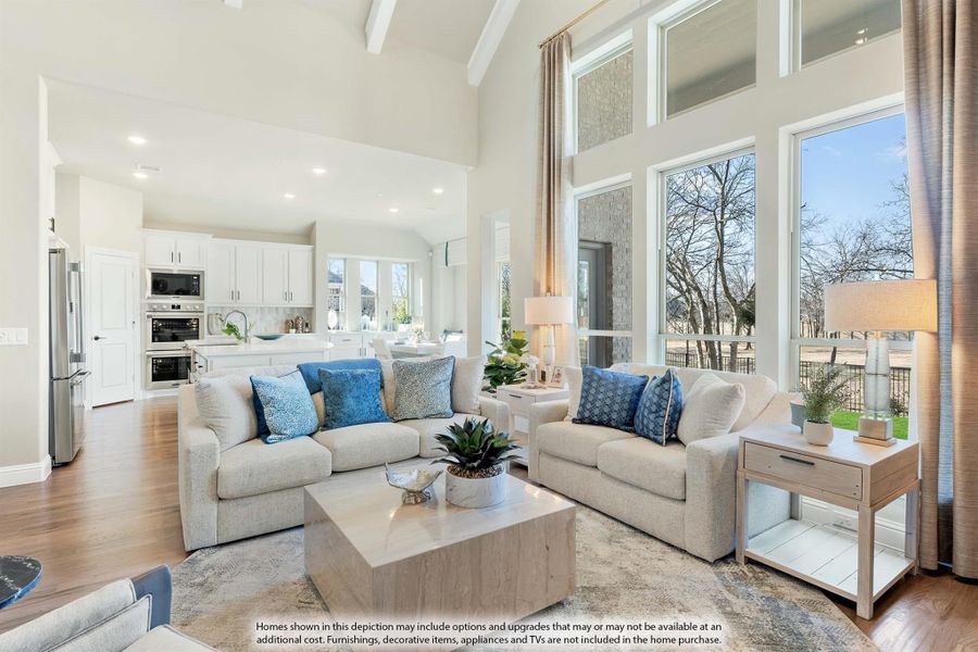 Open-concept living room with vaulted ceiling, two sofas, and large windows overlooking a kitchen with white cabinets. Open-concept living room with vaulted ceiling, two sofas, and large windows overlooking a kitchen with white cabinets.