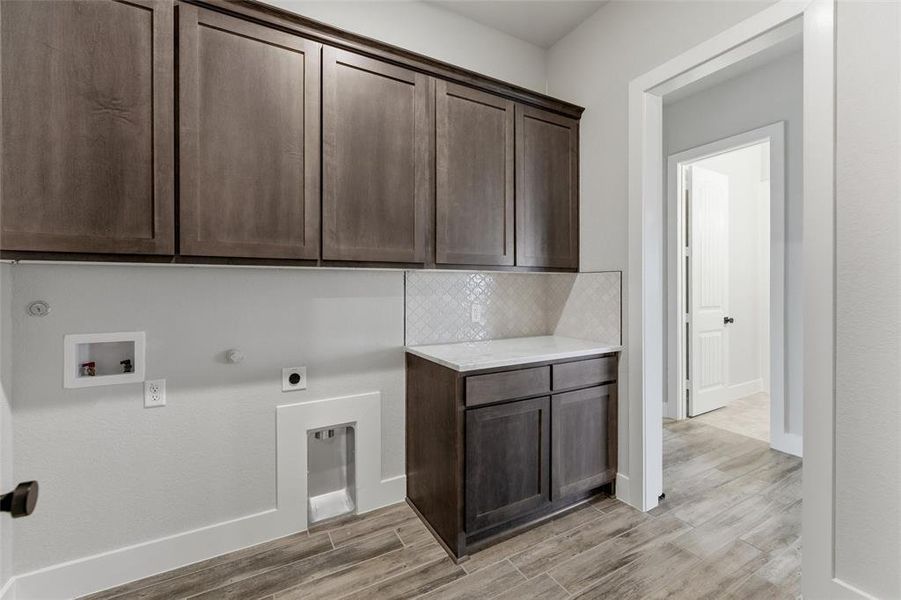 Laundry area featuring wood-finish flooring, dark wood cabinetry, a white countertop, and a white tile backsplash