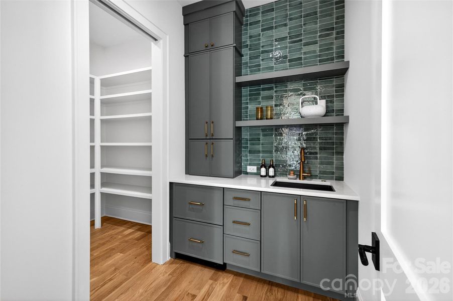 Walk-in Wet Bar. Beautiful glass tile backsplash. Drawers on bottom left are a refrigerator drawer and an ice drawer. Sink. To the left is the walk-in pantry with permanent shelves.