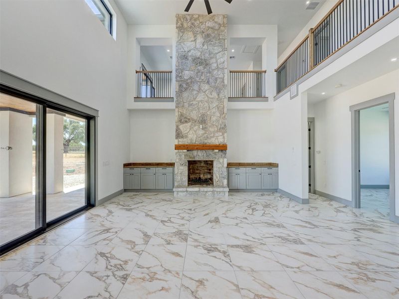 Double-height ceilings frame a towering stone fireplace in this light-filled room with marble-patterned tile flooring.