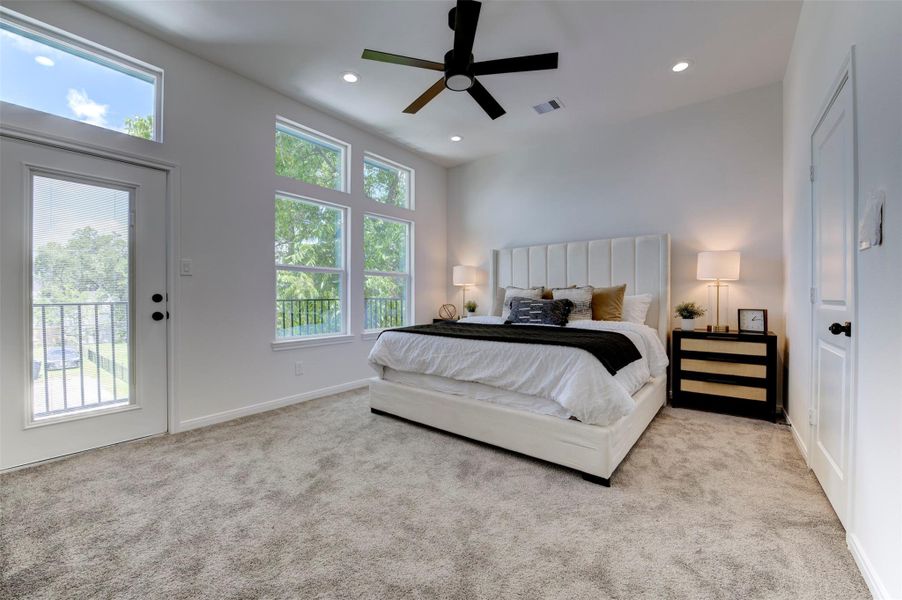 Spacious primary bedroom with direct balcony access, dual windows with tree views, recessed lighting, ceiling fan, and plush carpet throughout.