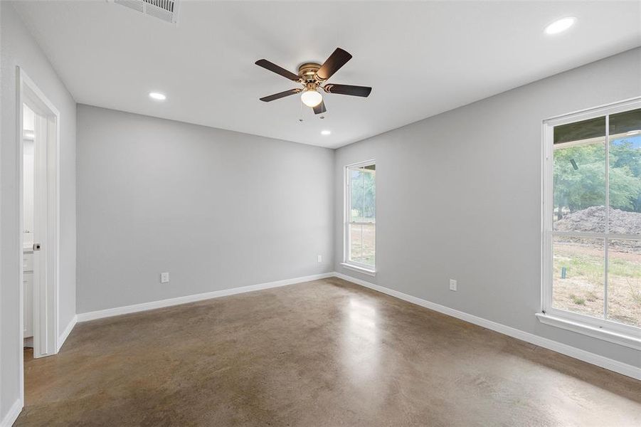 Empty room with finished concrete flooring, visible vents, a healthy amount of sunlight, and baseboards