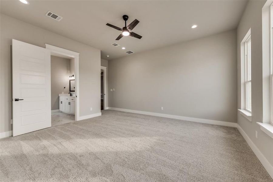 Unfurnished bedroom featuring ceiling fan, ensuite bathroom, and light carpet