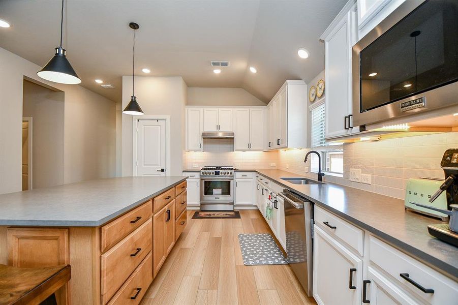 This modern kitchen features sleek countertops, ample cabinetry, and stainless steel appliances. It includes a spacious island with pendant lighting, providing an open and inviting space perfect for cooking and entertaining.