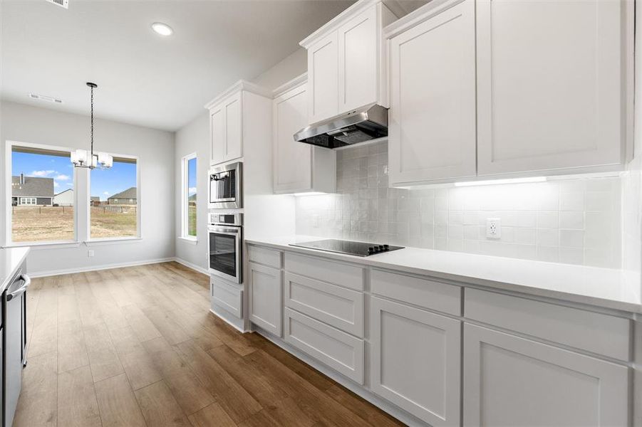 Kitchen featuring white cabinets, a chandelier, pendant lighting, under cabinet range hood, and stainless steel appliances Kitchen featuring white cabinets, a chandelier, pendant lighting, under cabinet range hood, and stainless steel appliances