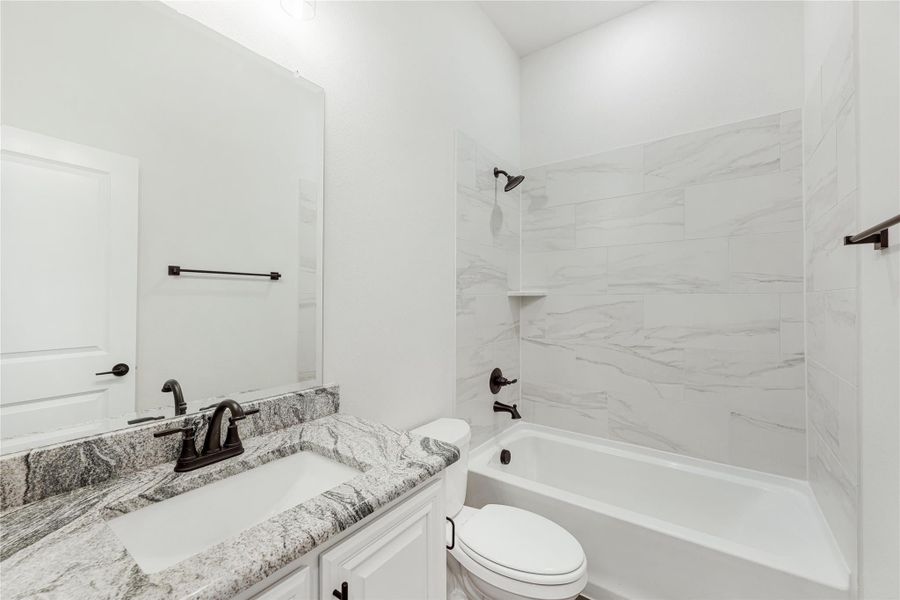 Bathroom with granite countertop vanity, white tub, and marble-tile shower surround with dark bronze fixtures Bathroom with granite countertop vanity, white tub, and marble-tile shower surround with dark bronze fixtures