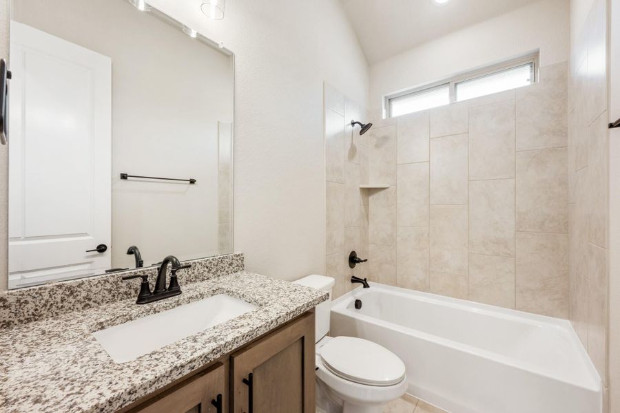 Bathroom with granite vanity, dark fixtures, toilet, and tiled tub-shower combo with small window above Bathroom with granite vanity, dark fixtures, toilet, and tiled tub-shower combo with small window above