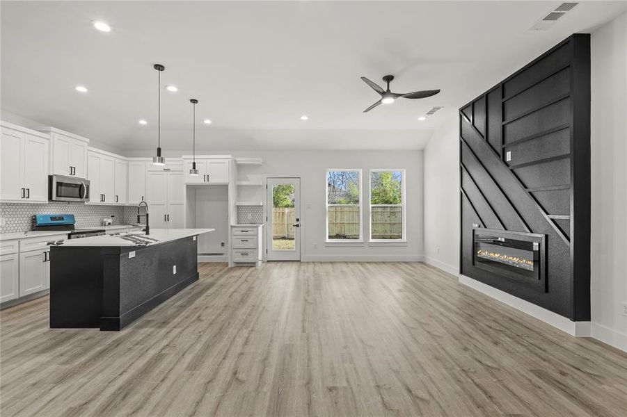 Kitchen featuring white cabinetry, hanging light fixtures, tasteful backsplash, a kitchen island with sink, and range